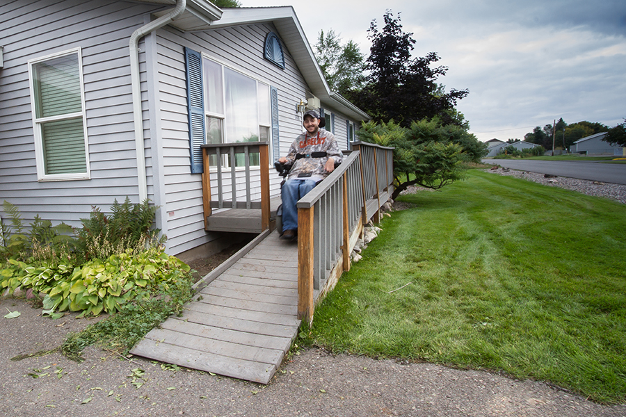 The man faces the viewer from the top of the ramp, smiling. He is wearing a camo sweatshirt that says Cabelas and blue jeans.